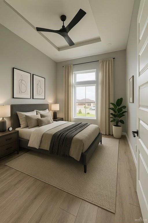 Bedroom featuring light wood finished floors, a tray ceiling, ceiling fan, and baseboards