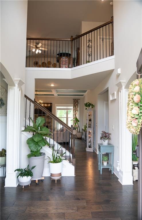 Foyer with ornate columns, a towering ceiling, stairway, arched walkways, and wood finished floors