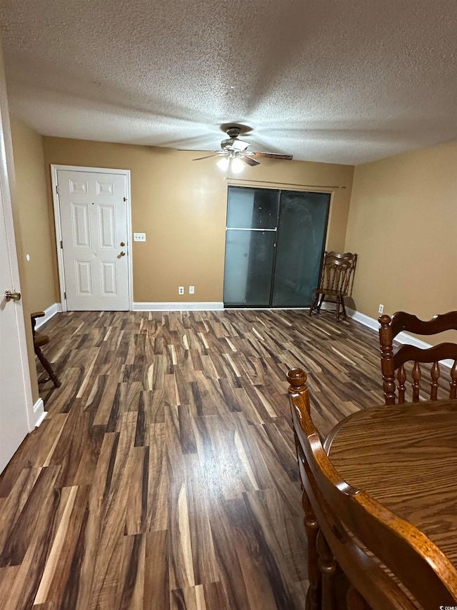 Living room featuring dark wood-style flooring, a textured ceiling, and ceiling fan
