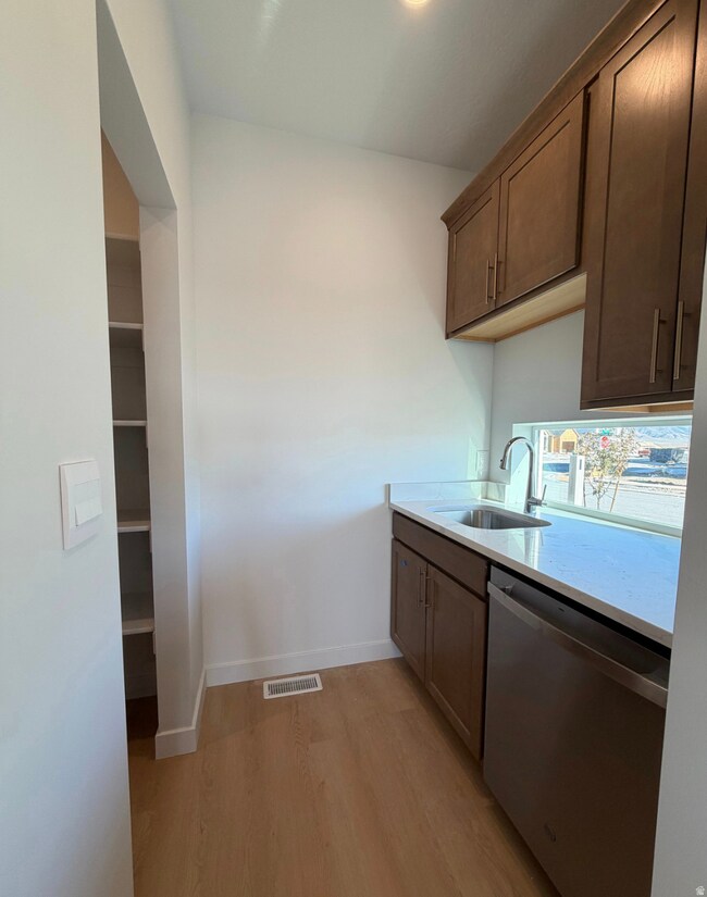 Kitchen featuring light wood-style floors, dishwasher, light stone countertops, and dark brown cabinets