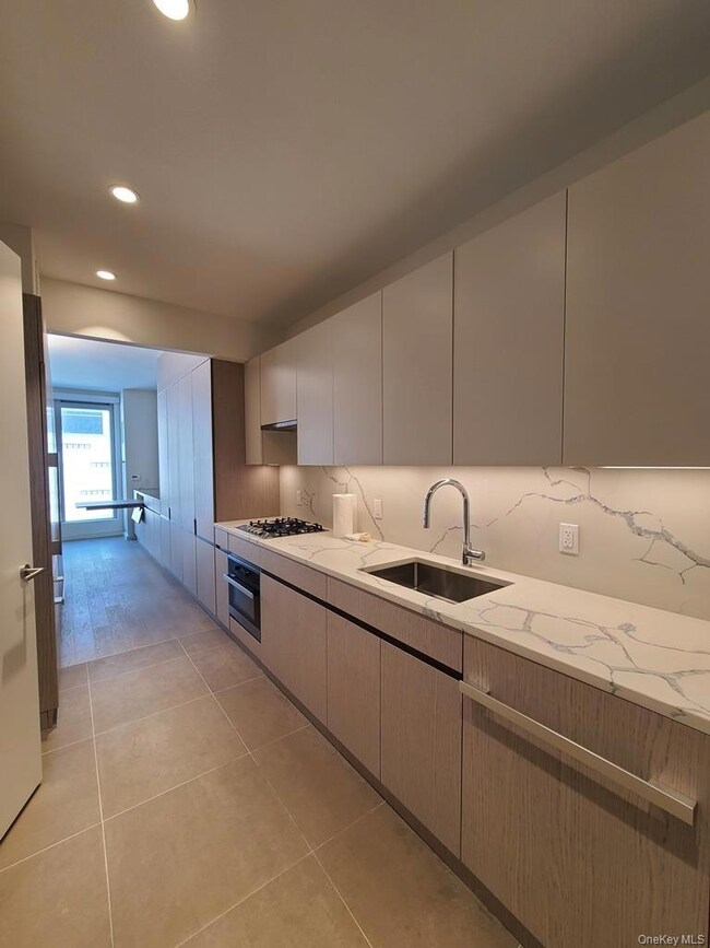 Kitchen featuring modern cabinets, recessed lighting, backsplash, light stone countertops, and light tile patterned floors