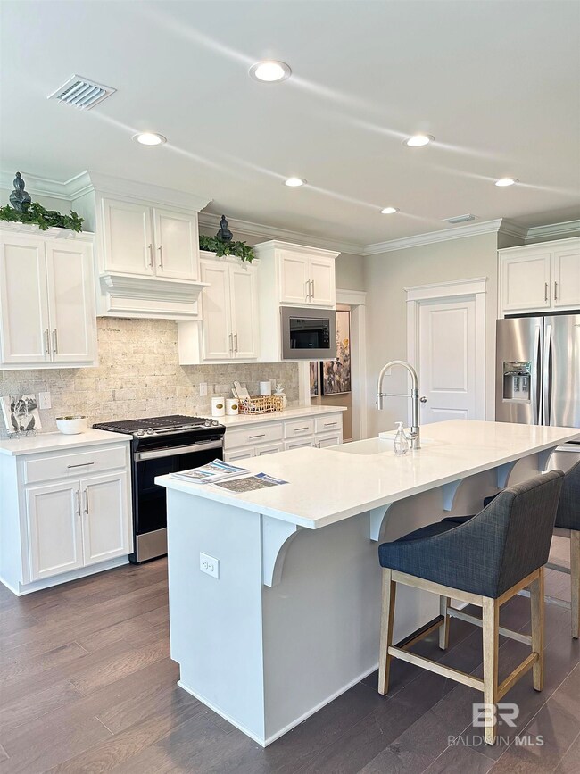 Kitchen featuring appliances with stainless steel finishes, a kitchen island with sink, dark wood-type flooring, and tasteful backsplash