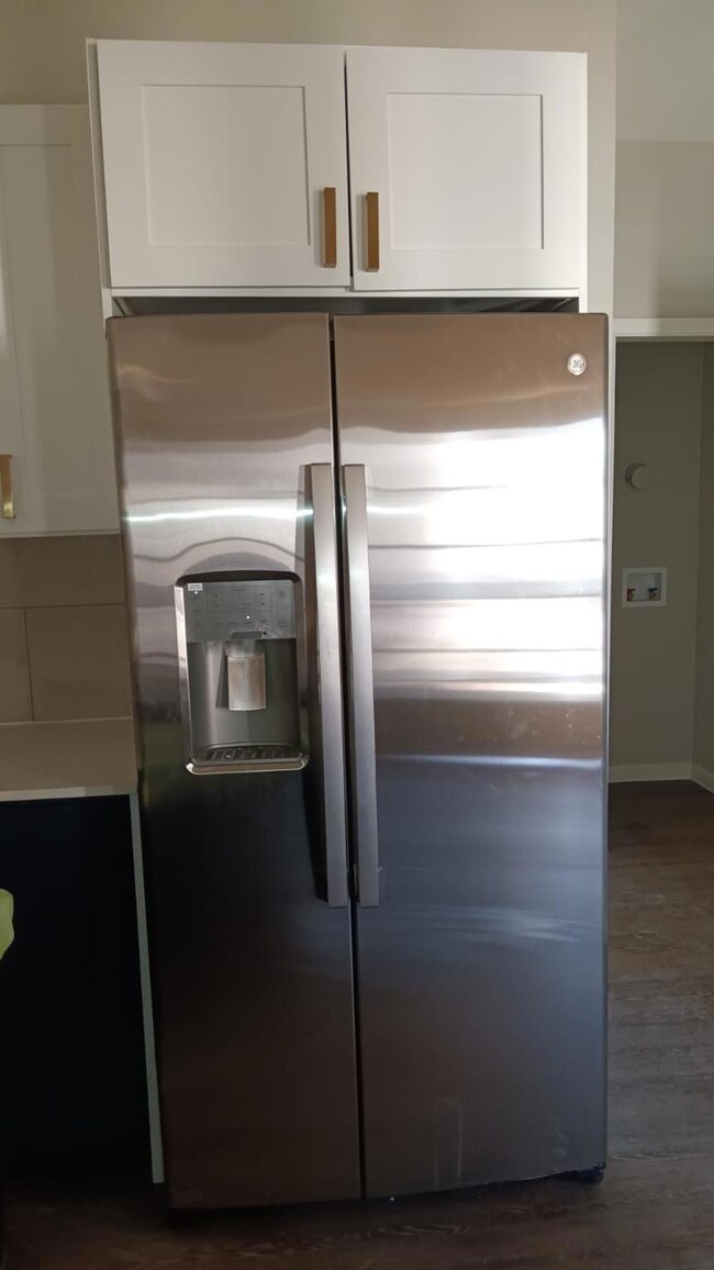 Kitchen view of stainless steel refrigerator with ice dispenser, white cabinetry, dark wood-style flooring, and light countertops