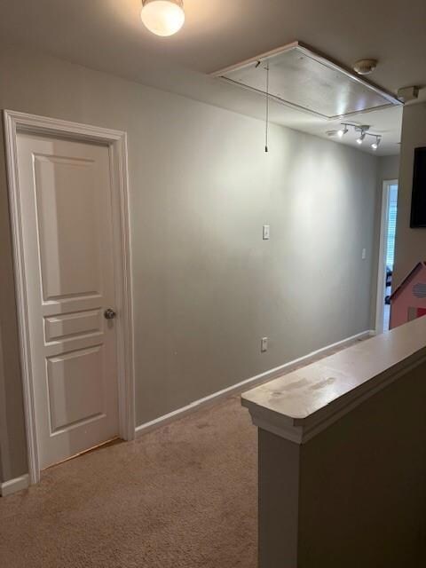 Carpeted empty room featuring a smoke detector, track lighting, and attic access