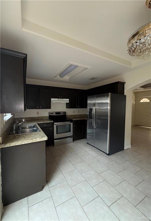 Kitchen with light tile patterned floors, a sink, under cabinet range hood, appliances with stainless steel finishes, and dark cabinetry