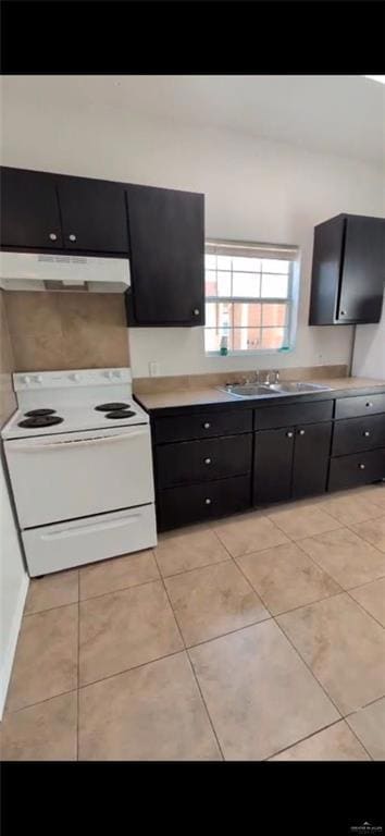 Kitchen featuring white range with electric cooktop, under cabinet range hood, a sink, dark cabinetry, and light countertops