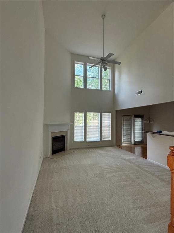 Unfurnished living room with a towering ceiling, ceiling fan, carpet flooring, baseboards, and a fireplace