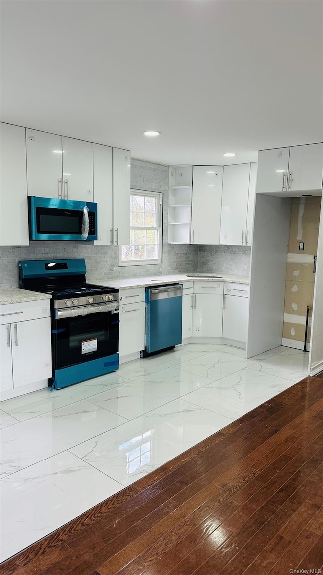 Kitchen with stainless steel appliances, white cabinetry, decorative backsplash, and open shelves