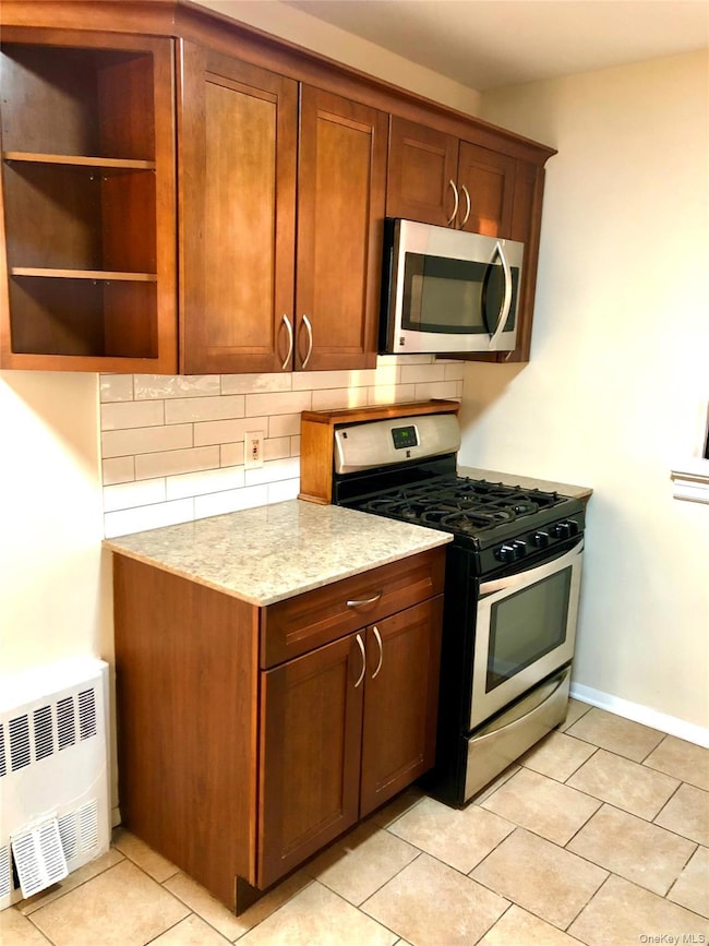 Kitchen featuring appliances with stainless steel finishes, decorative backsplash, light tile patterned floors, light stone counters, and radiator