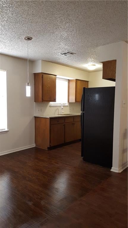 Kitchen with freestanding refrigerator, brown cabinets, a textured ceiling, dark wood-style flooring, and light countertops
