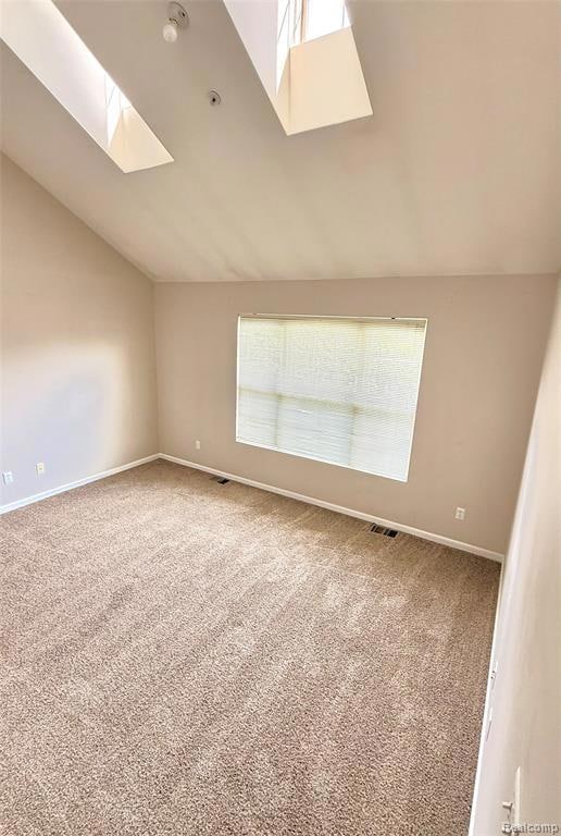Carpeted empty room with vaulted ceiling and a skylight