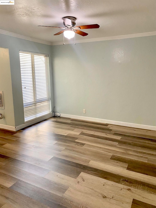 Living room featuring a ceiling fan, laminate wood floors, crown molding, and baseboards