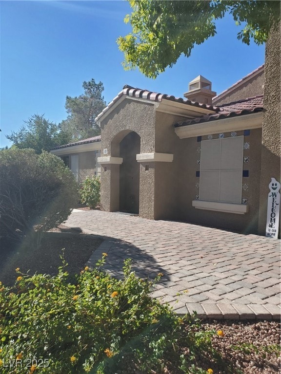 View of front of home featuring stucco siding, a tiled roof, and a chimney