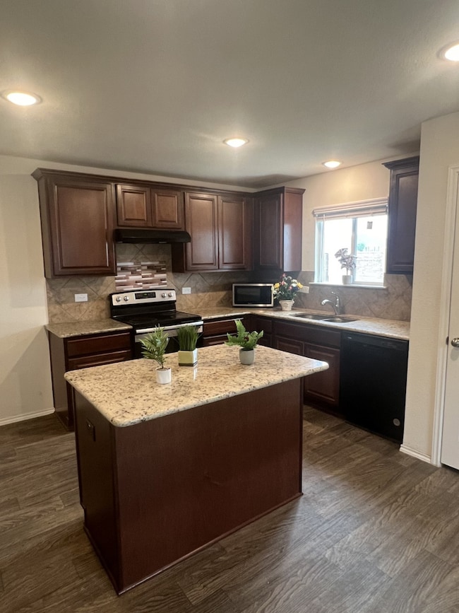 Kitchen with appliances with stainless steel finishes, dark brown cabinetry, decorative backsplash, a center island, and recessed lighting