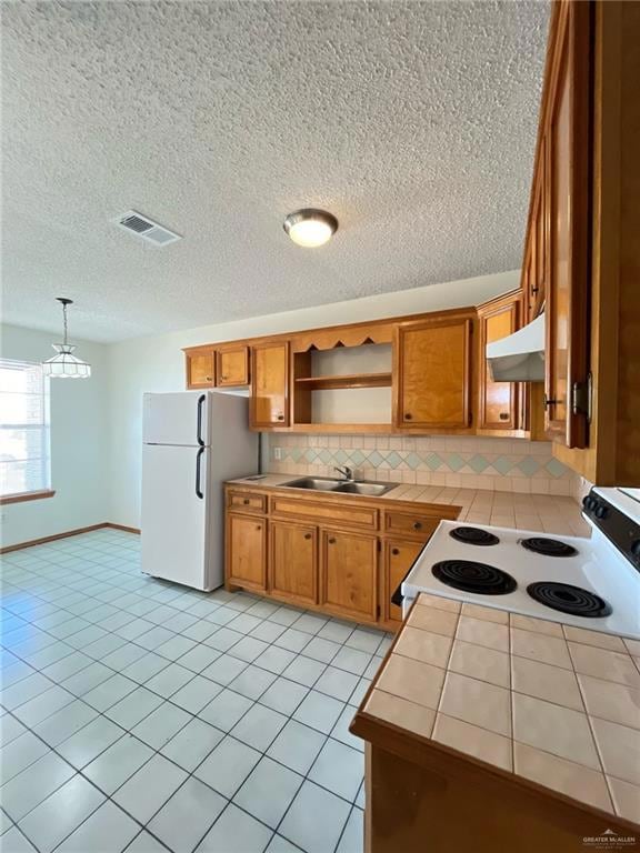 Kitchen featuring tile counters, brown cabinetry, white appliances, backsplash, and a textured ceiling