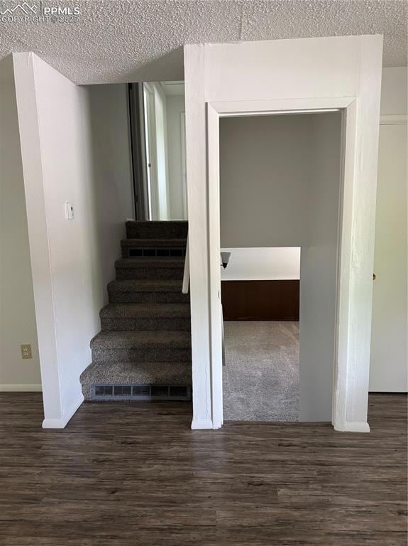 Stairs with a textured ceiling, wood finished floors, and baseboards