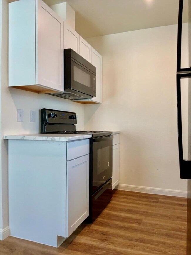 Kitchen featuring black appliances, light countertops, white cabinets, and light wood-type flooring