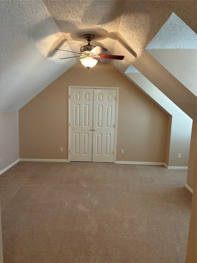 Additional living space with a textured ceiling, light carpet, vaulted ceiling, and a ceiling fan