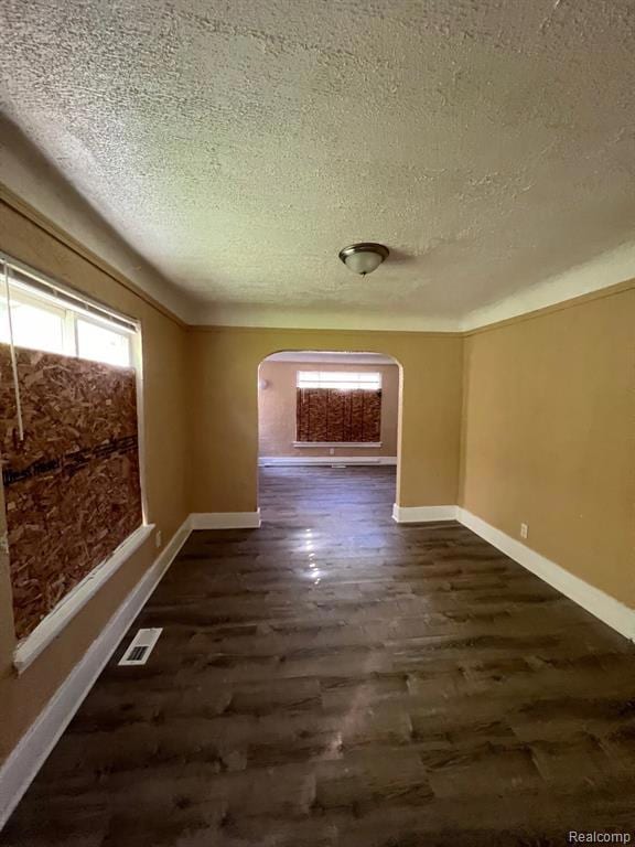 Empty room with arched walkways, dark wood-style flooring, and a textured ceiling