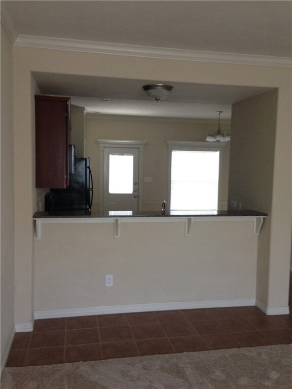 Kitchen with kitchen peninsula, a breakfast bar, dark tile patterned floors, and ornamental molding