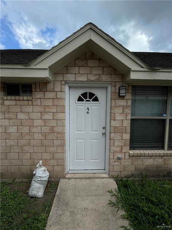 Property entrance with a shingled roof and brick siding