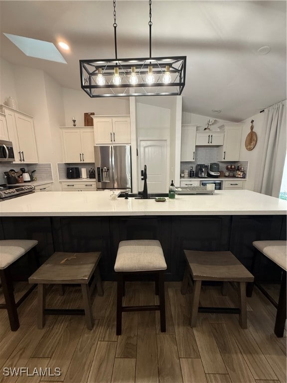 Kitchen featuring backsplash, white cabinetry, a skylight, and a kitchen breakfast bar