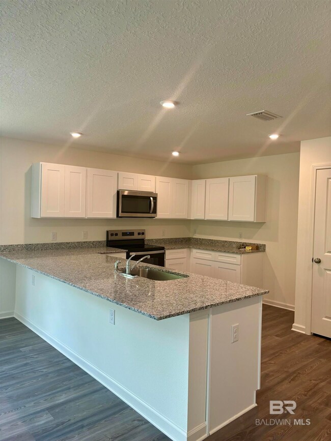 Kitchen featuring stainless steel appliances, dark hardwood / wood-style flooring, white cabinets, sink, and kitchen peninsula