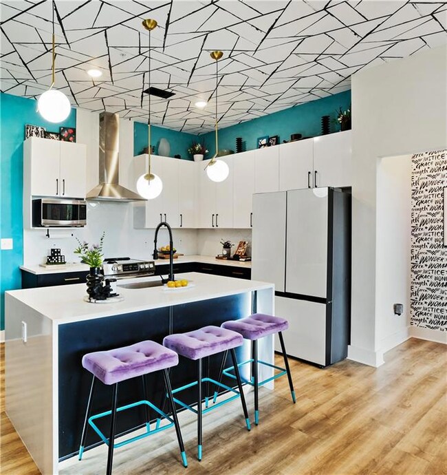 Kitchen featuring freestanding refrigerator, wall chimney range hood, a sink, stainless steel microwave, and decorative light fixtures