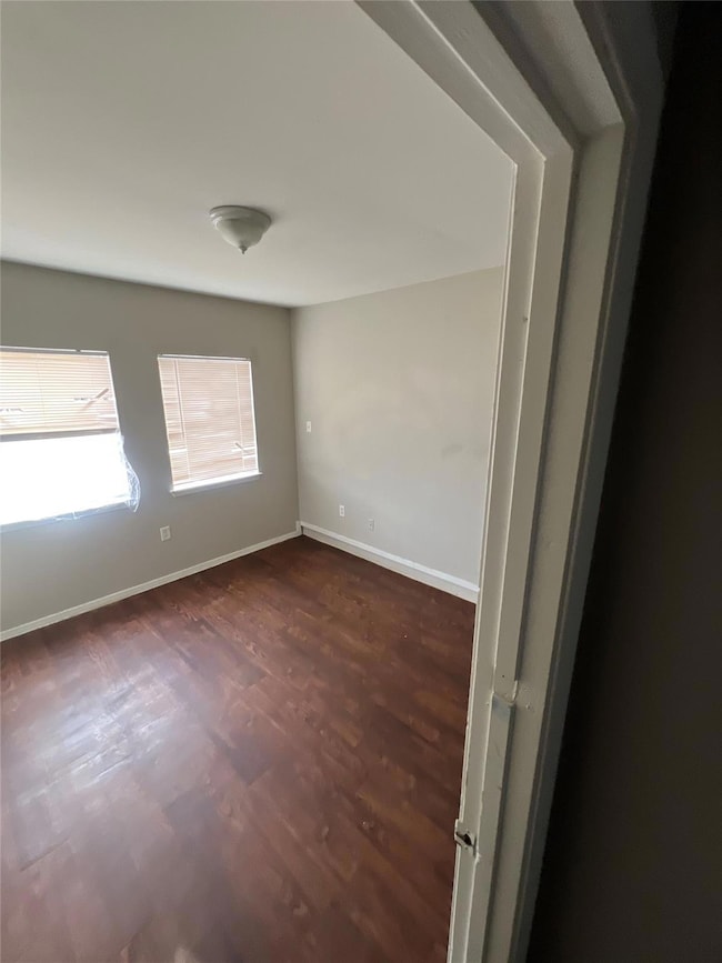 Empty room featuring dark wood-style flooring and baseboards