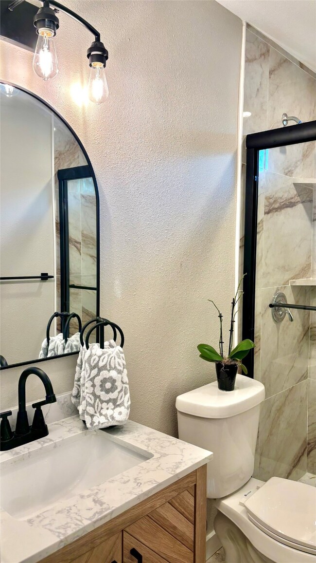 Full bathroom featuring a textured wall, vanity, and a stall shower