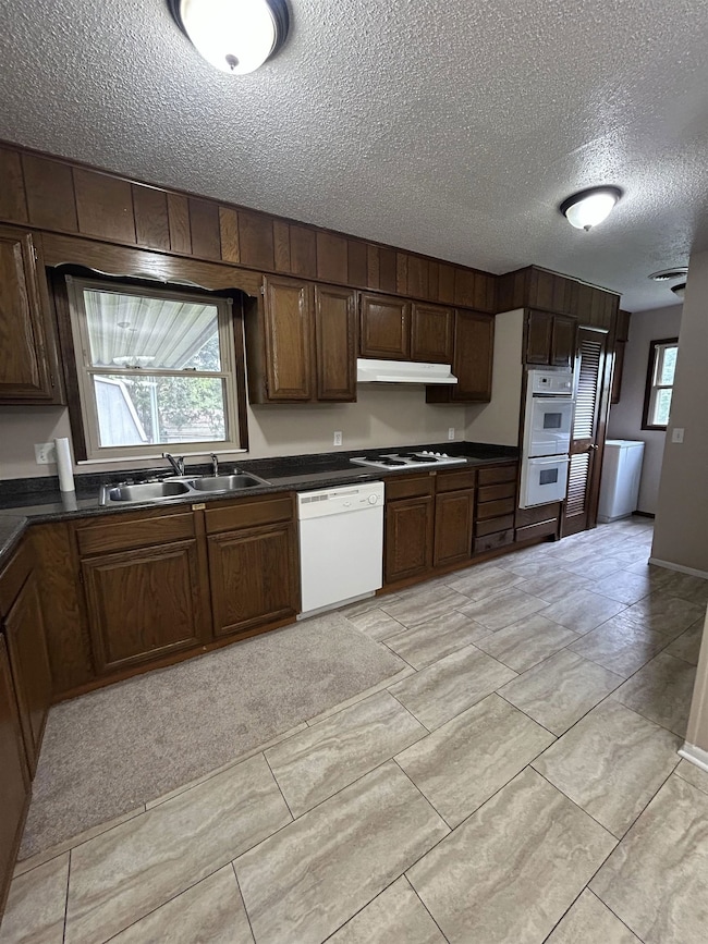 Kitchen featuring white appliances, a sink, dark c