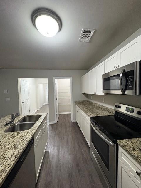 Kitchen featuring stainless steel appliances, dark wood-type flooring, light stone counters, and white cabinets