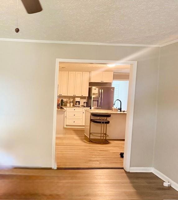 Kitchen featuring stainless steel fridge with ice dispenser, crown molding, a kitchen bar, light wood-type flooring, and light countertops