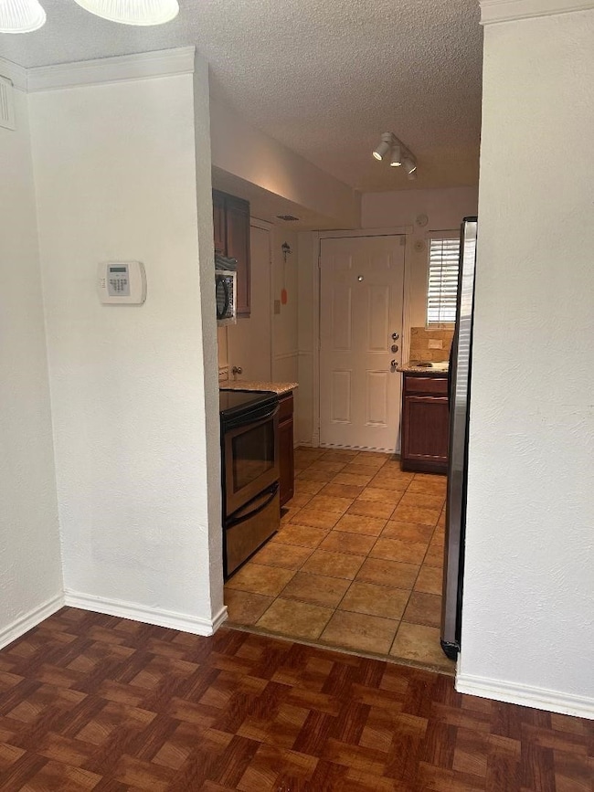Hallway with a textured ceiling, dark tile patterned flooring, and a textured wall