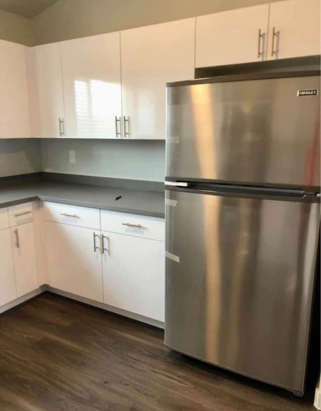 Kitchen with freestanding refrigerator, white cabinetry, dark wood-style floors, and dark countertops