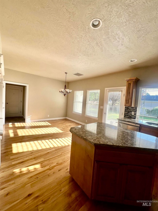 Kitchen featuring dark stone countertops, hanging light fixtures, a textured ceiling, light wood floors, and healthy amount of natural light