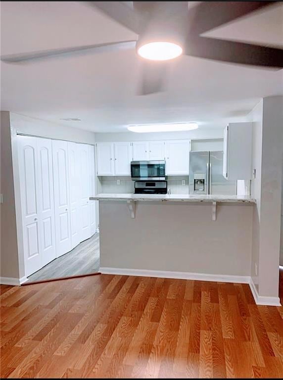 Kitchen featuring stainless steel appliances, a kitchen bar, light countertops, and light wood finished floors