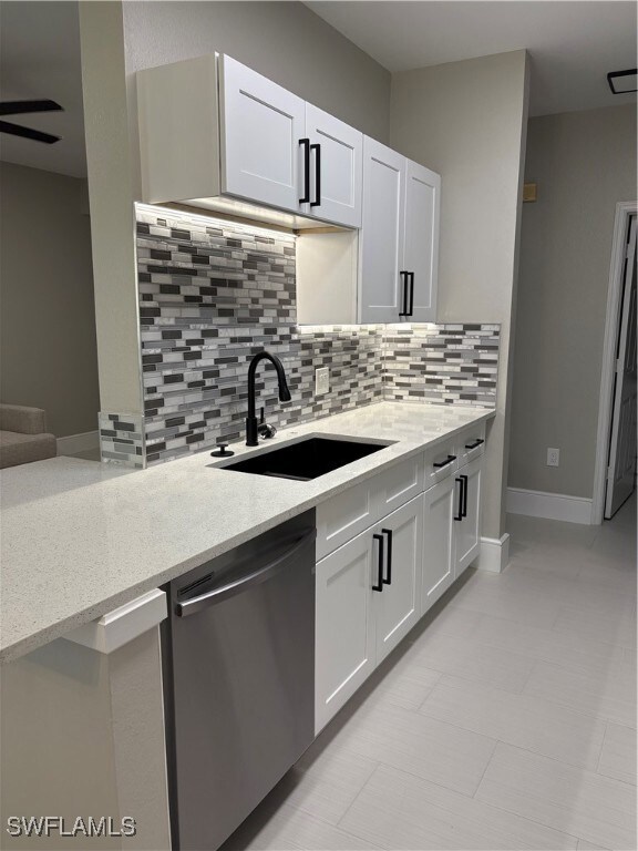 Kitchen featuring decorative backsplash, dishwashing machine, light stone counters, and white cabinetry