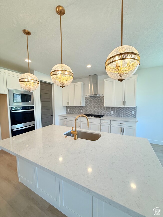 Kitchen featuring white cabinets, light wood-style floors, tasteful backsplash, decorative light fixtures, and a large island with sink