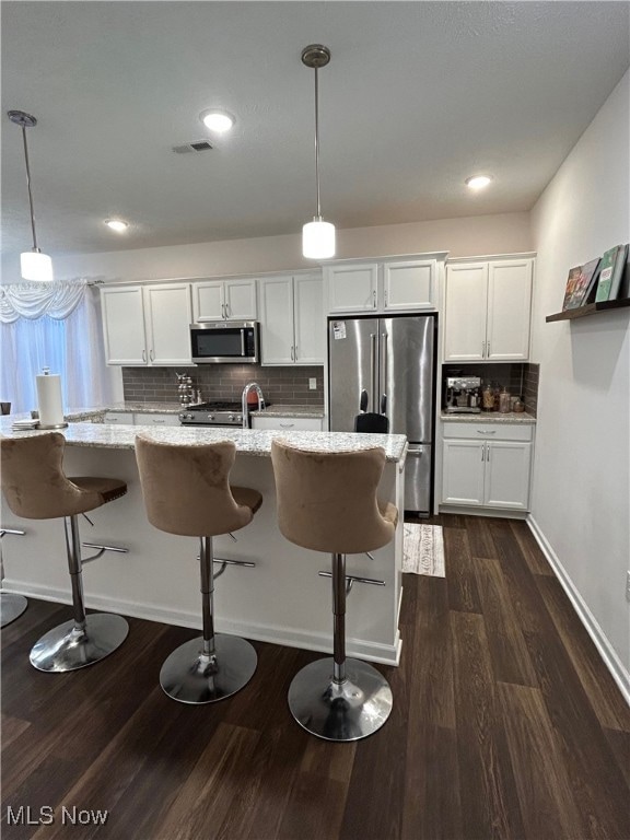Kitchen with white cabinets, a breakfast bar, light stone countertops, backsplash, and appliances with stainless steel finishes