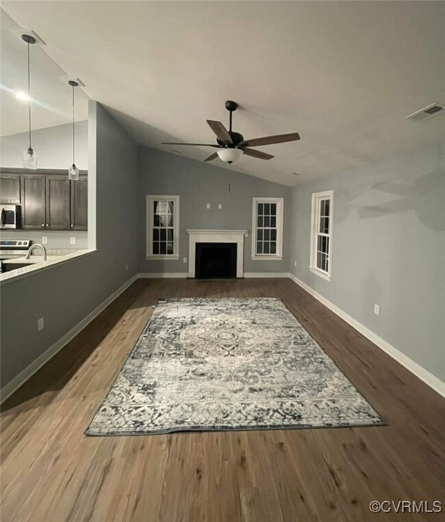 Unfurnished living room featuring vaulted ceiling, ceiling fan, and dark wood-type flooring