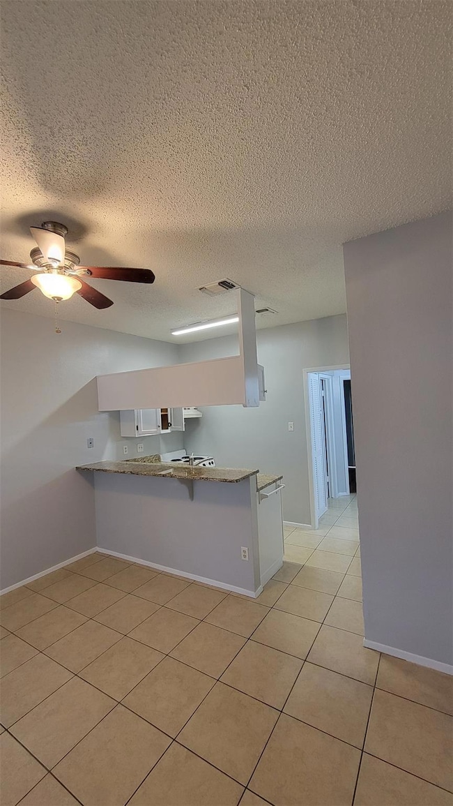 Kitchen featuring a textured ceiling, ceiling fan, light tile patterned floors, a peninsula, and white cabinets