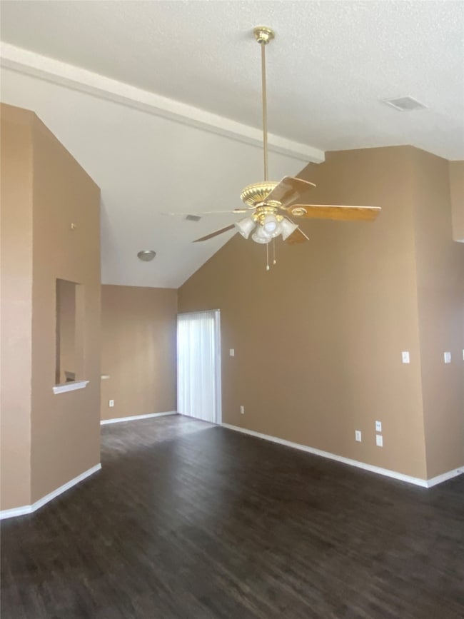 Empty room featuring beam ceiling, dark wood-style flooring, a ceiling fan, and high vaulted ceiling