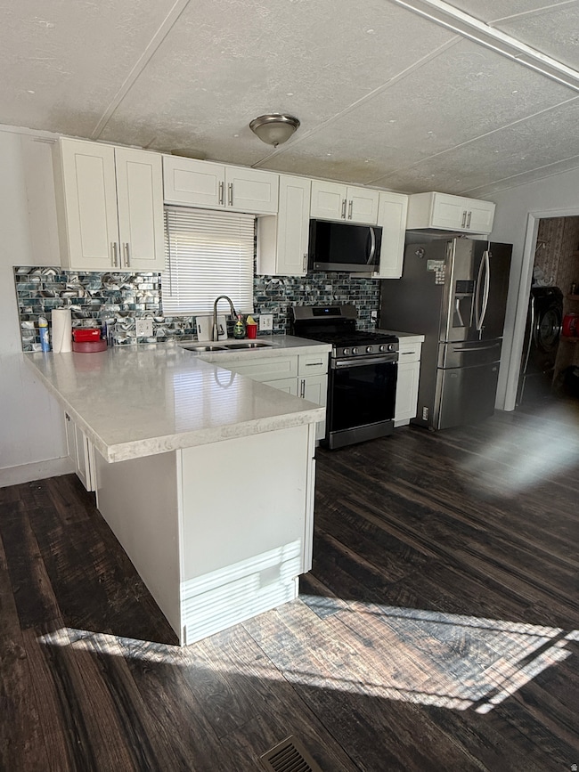 Kitchen featuring a peninsula, white cabinets, stainless steel appliances, decorative backsplash, and dark wood-style flooring