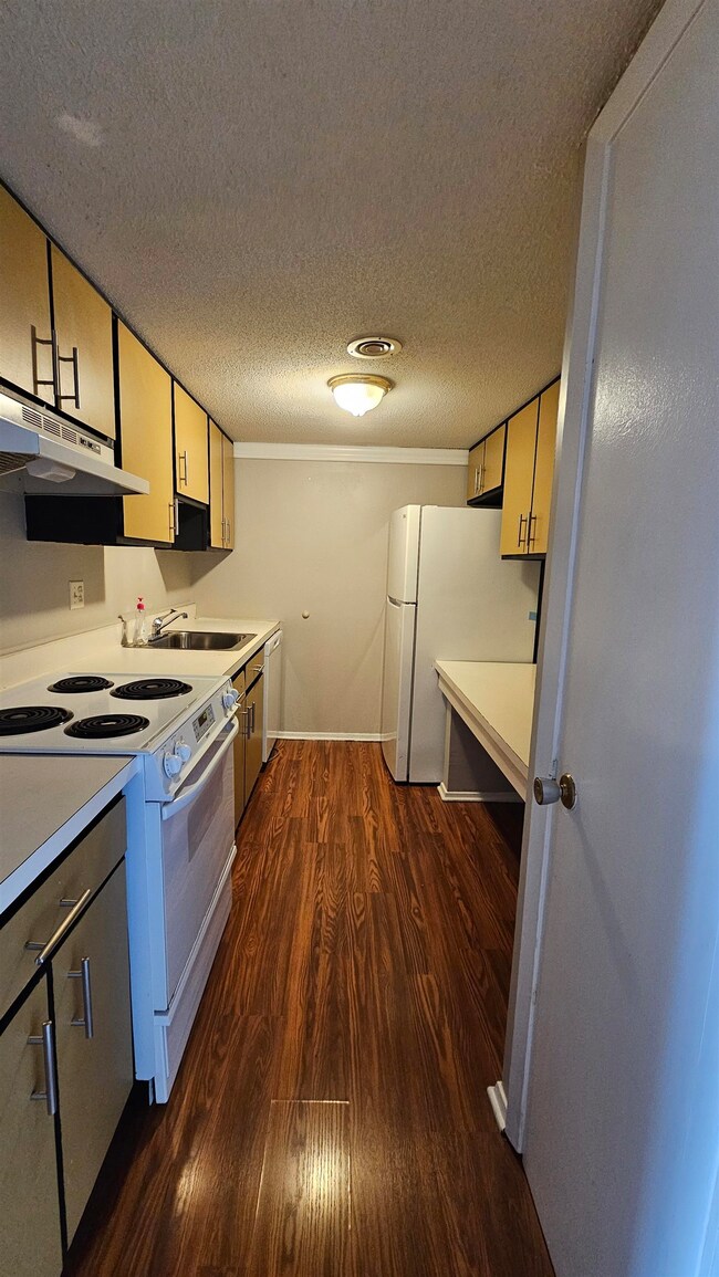 Kitchen with white appliances, exhaust hood, dark wood-style floors, light countertops, and a textured ceiling