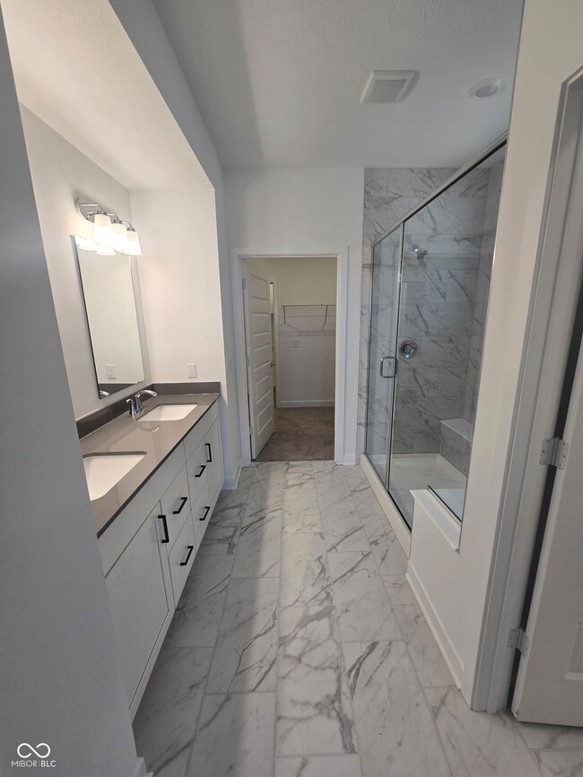 full bath featuring marble look tile flooring, double vanity, a marble finish shower, and a spacious closet
