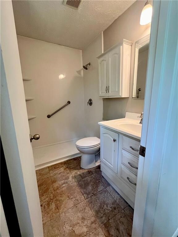 Full bathroom with vanity, toilet, a textured ceiling, and a shower