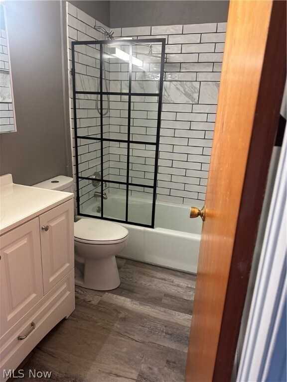 Full bathroom featuring hardwood / wood-style floors, combined bath / shower with glass door, toilet, and vanity