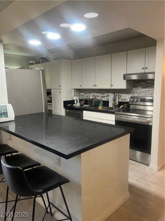 Kitchen featuring range, backsplash, light wood-style floors, a breakfast bar area, and fridge