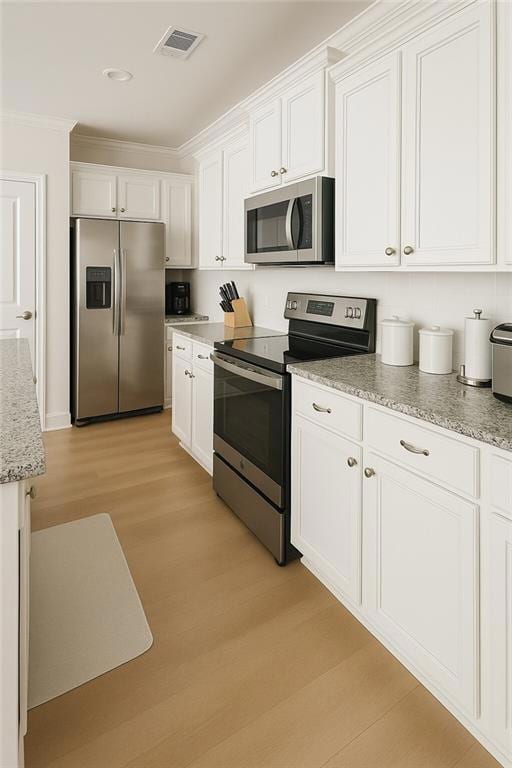 Kitchen featuring appliances with stainless steel finishes, light wood-style floors, white cabinetry, crown molding, and light stone counters